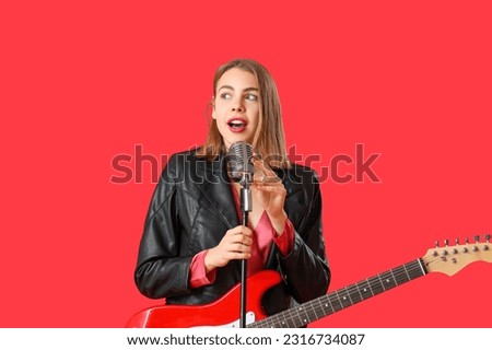 Young woman with guitar and microphone singing on red background