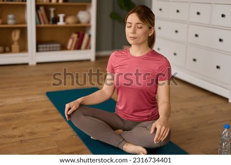 Beautiful young woman meditating on yoga mat at home