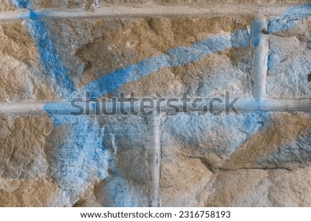 A close up photo of blue and white graffiti that has been sprayed onto an orange limestone brick wall.