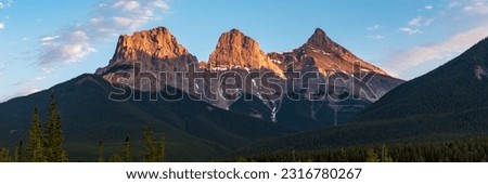Golden sunset peaks near Banff National Park with Three Sisters at Canmore in view. Sun shining bright on the stunning panoramic view of wilderness, nature scenery in Canada. Royalty-Free Stock Photo #2316780267