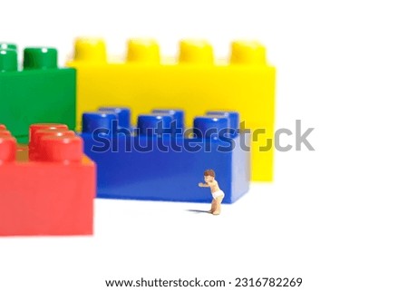 Miniature people toy figure photography. Sensory and motor development. A boy toddler walking toward colorful brick. Isolated white background. Image photo