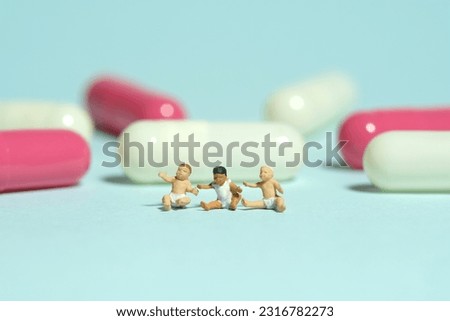 Miniature tiny people toy figure photography. Group of infant baby seat in front of medicine pill tablet capsule. Isolated on blue background. Image photo