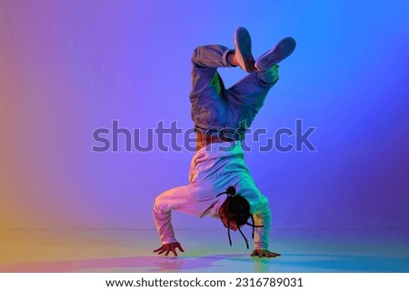 Flexible young man, contemp dancer performing breakdance, hip-hop against gradient multicolored studio background in neon light. Concept of street style dance, fashion, youth, hobby, dynamics, ad Royalty-Free Stock Photo #2316789031