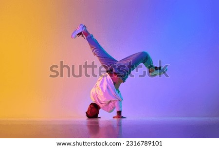 Creative young guy in casual clothes dancing hip-hop contemporary, breakdance against gradient studio background in neon light. Concept of street style dance, fashion, youth, hobby, dynamics, ad