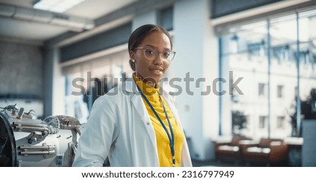 Portrait of Young Smiling Black Woman Wearing Glasses and a Lab Coat Looking at the Camera. Future Engineer Pursuing Scientific Career. Industrial Manufacturing Student in University Laboratory Posing Royalty-Free Stock Photo #2316797949