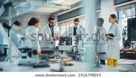 Diverse Team of Industrial Robotics Specialists Gathered Around a Table With a Mobile Robot. Engineers In Lab Coats Discussing an Automated AI Robotic Delivery Assistant, Using Laptop and Tablet Royalty-Free Stock Photo #2316798019
