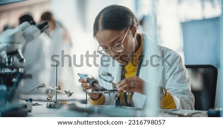 Portrait of Black Female Lab Specialist Carefully Soldering a Circuit Board in a Manufacturing Industrial Company. Professional Woman in Lab Coat Working on the Latest Technological Project Royalty-Free Stock Photo #2316798057