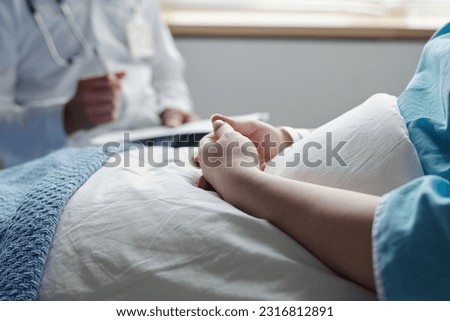 Close-up of hands of young woman with oncological disease sitting under blanket in bed and consulting with her doctor after medical treatment Royalty-Free Stock Photo #2316812891