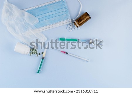 Top view of syringes, blue hygienic protective mask, gloves, tablets and glass medicine bottle ready for use. Pandemic and health concept.