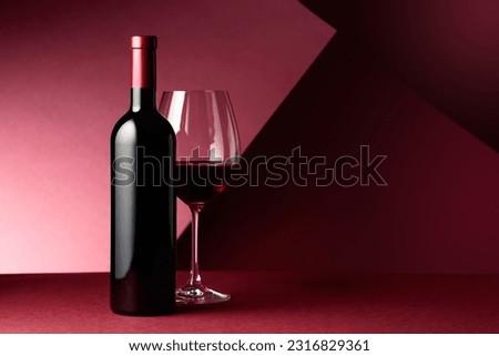 Bottle and glass of red wine on a red background. Copy space. Royalty-Free Stock Photo #2316829361