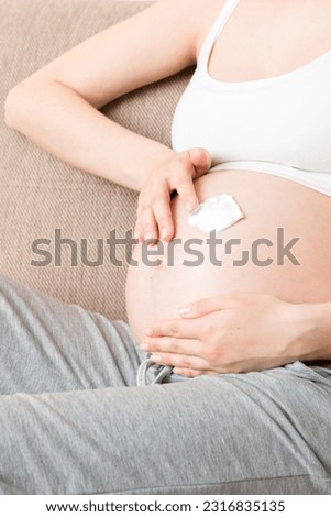 a pregnant girl sits at home on the bed and smears an anti-stretch mark cream on her stomach. Pregnancy, motherhood, preparation and expectation concept.
