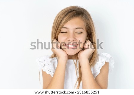 beautiful caucasian teen girl wearing white blouse over white wall grins joyfully, imagines something pleasant, copy space. Pleasant emotions concept.