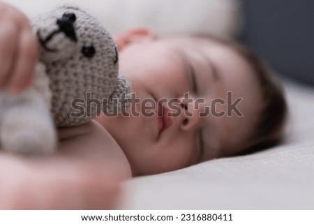 Chubby baby boy with closed eyes sleeping in crib on soft white sheet hugging knitted bear adorable kid resting with toy in nursery at home after breastfeeding closeup Royalty-Free Stock Photo #2316880411