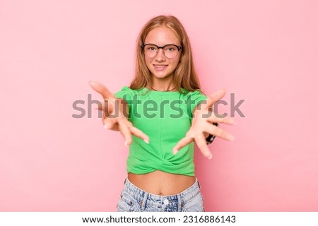 Caucasian teen girl isolated on pink background feels confident giving a hug to the camera.