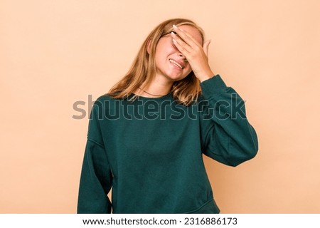 Caucasian teen girl isolated on beige background laughs joyfully keeping hands on head. Happiness concept.