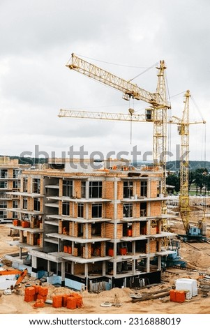 vertical photo of two cranes near building. Concrete building under construction