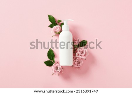 White shampoo bottle mockup with rose blossoms on pink background. Flat lay, top view.