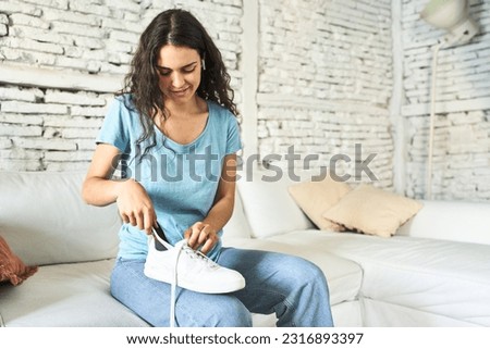 A young Caucasian woman, seated on the sofa, gently placing an orthopedic insole into her shoe, seeking comfort and foot support.