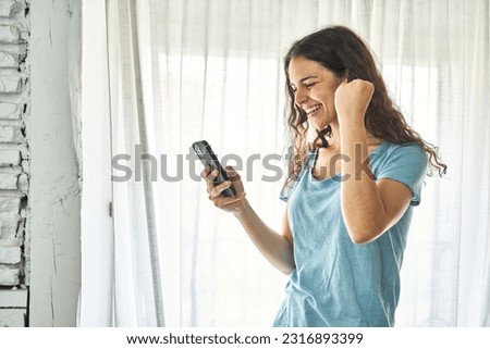 A young Caucasian woman, joyfully reading good news on her phone, celebrating a moment of happiness and fulfillment. Royalty-Free Stock Photo #2316893399