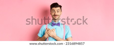 Cheerful young man with moustache, wearing shirt and bow-tie, holding hands on heart and smiling grateful, saying thank you, standing on pink background. Royalty-Free Stock Photo #2316894857