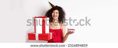 Happy birthday girl in red dress, celebrating and holding gifts with bday cake, standing on white background.