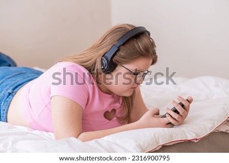 Concentrated teenage girl in headphones listens to podcast while writing messages to friend schoolgirl in glasses enjoying modern technology at home after classes