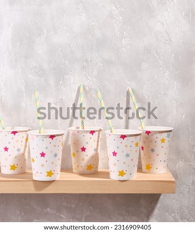 Pattern of white holiday paper drinking cups with pictures of colorful stars with straws on a wooden surface. Copy space for text. Holiday fun party.