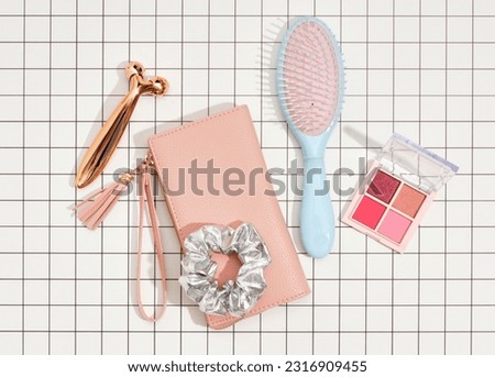 Women's pink wallet for money or business cards, eye shadow for fashionable and stylish makeup, hair comb, roller facial massager. Top view of make up acessories.