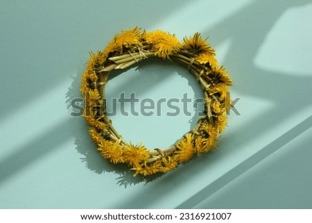 Dandelion wreath on light blue background. Summer sun casts intresting shadows on the picture. Summer vibes.