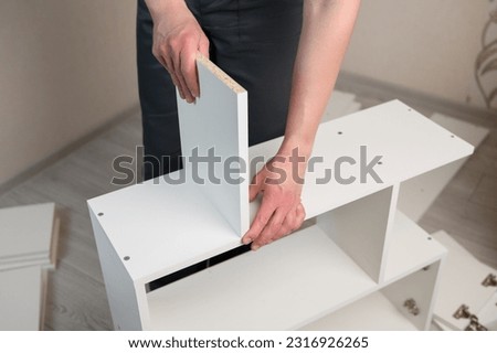 Furniture assembly. The furniture assembler takes a white shelf, tightens the screw with a hex wrench.Collector of furniture.Moving concept, furniture assembler, self assembly Royalty-Free Stock Photo #2316926265