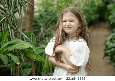 Offended sad little blonde girl in the botanical garden. a girl in a white dress exploring tropical plants and flowers in the greenhouse.