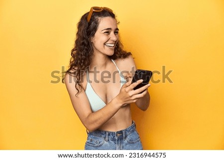 Woman laughing at phone content, vivacious yellow scene.
