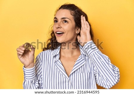 Woman holding a physical Bitcoin coin, trying to listening a gossip. Royalty-Free Stock Photo #2316944595
