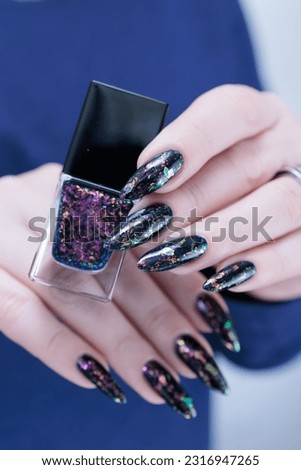 Woman's beautiful hand with long nails and dark blue manicure with bottles of nail polish