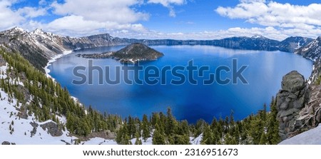 Crater Lake - A panoramic cliff-side overview of deep blue Crater Lake, surrounded by the rugged lake rim, on a calm Spring day. Crater Lake National Park, Oregon, USA.