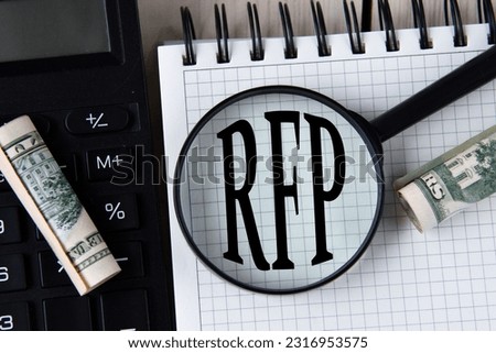 Letters RFP (Request for proposal) under a magnifying glass on a white notebook against the background of a fragment of a calculator and banknotes Royalty-Free Stock Photo #2316953575