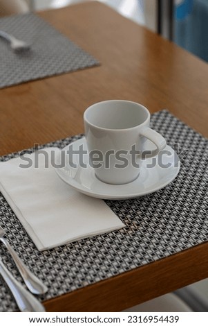 White coffee cup and saucer on a napkin on a kitchen wooden table. Soft selective focus. blurred  background, concept tea time, hobby.  Closeup of a white ceramic  mug with spoon on a white napkin.
