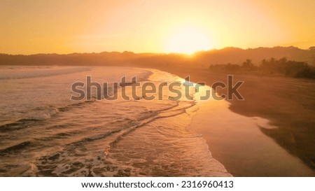 AERIAL: Golden morning sunbeams illuminating beautiful beach of Playa Venao. Picturesque surfing location with sandy shore and rolling waves of Pacific Ocean. Adventure tourism in amazing Panama.