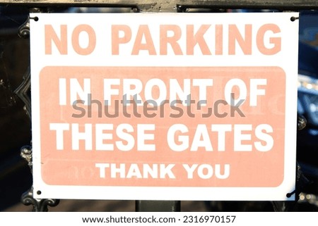 Worn White and red parking sign "No Parking in front of these gates Thank you"