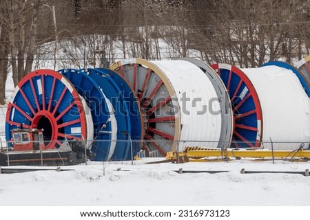 Bulk sub-sea industrial glass fiber optic cable on a metal spool on ship stands. The data line is coiled around large industrial reels in a storage yard.  Internet communications spool storage yard. Royalty-Free Stock Photo #2316973123