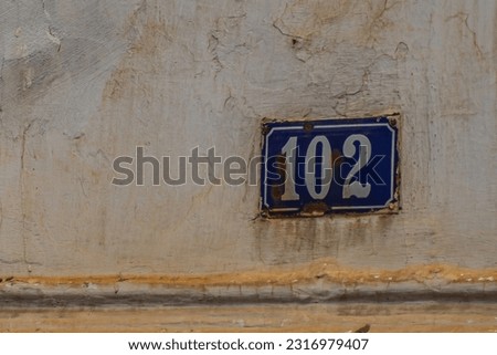 Оld, slightly dirty street sign indicating the house number. The coating of the wall and the tablet, under the influence of time, became covered with cracks and rust. Concept of aging and destruction
