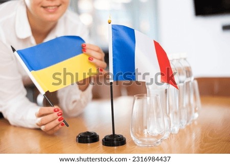 Young woman in business clothes puts flags of Ukraine and France on negotiating table in office