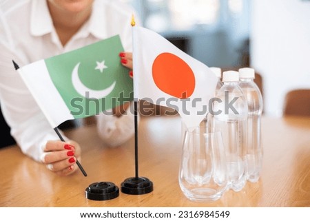 Little flag of Japan on table with bottles of water and flag of Pakistan put next to it by positive young woman in meeting room