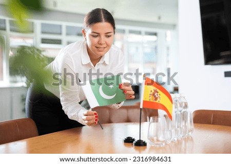 ..Young woman in business clothes puts flags of Pakistan and Spain on negotiating table in office..