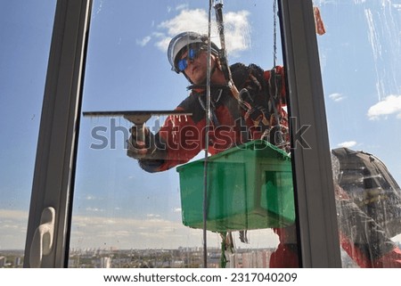 A blurry view through a dirty window of a window washer. Rope access. An alpinist washes windows Royalty-Free Stock Photo #2317040209