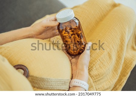 Prenatal Vitamins. Portrait Of Beautiful Smiling Pregnant Woman Holding Transparent Glass Jar With Pills, Taking Supplements For Healthy Pregnancy While Sitting On Couch At Home, Free Space Royalty-Free Stock Photo #2317049775