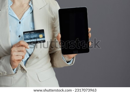 Closeup on small business owner woman in a light business suit with tablet PC and credit card isolated on gray.