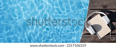 Book and headphones near swimming pool. Summer vacation. Flat lay with copy space Royalty-Free Stock Photo #2317106319