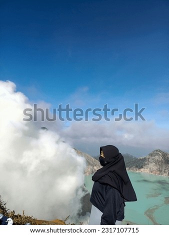 A black-hijab-clad woman on a mountain peak, her silhouette against the blue sky. Strength, serenity, and faith intertwined in nature's beauty.