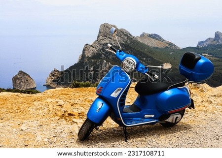 Blue motor scooter on coastal road with sea and rocks in background. High quality photo Royalty-Free Stock Photo #2317108711